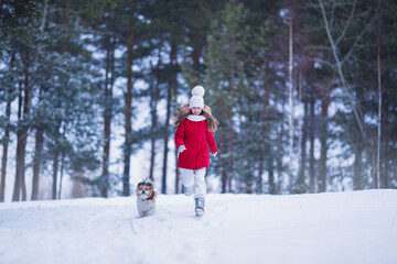 Fototapeta na wymiar Lovely joyful girl running with a dog in the winter forest