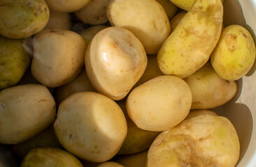 Young peeled potatoes lie in a pot of water. View from above