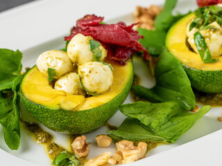 Bocconcini cheese balls in halves of avocado served with salad on white plate