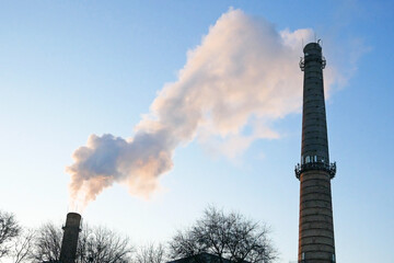 plant tubes with gray smoke on blue sky, chemical plant towers of nuclear power plant against the...