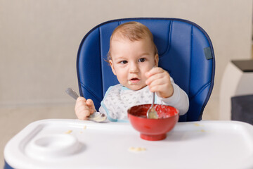 The grimy infant or toddler tries to eat independently. Baby-led weaning. Little child eats himself with a spoon.