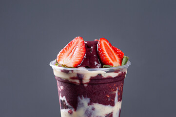 Brazilian frozen açaí in a plastic cup with condensed milk and strawberry. Fruit from the Amazon.