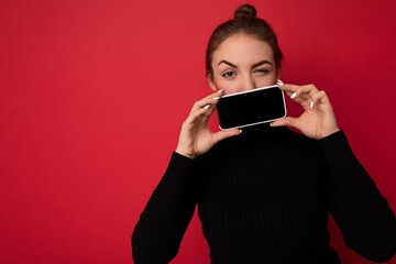 Photo of attractive winking young brunette woman wearing black sweater standing isolated over red...