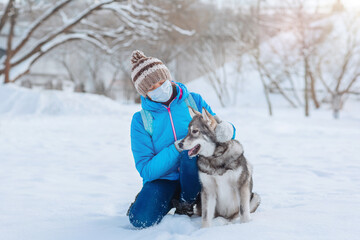 Alone woman wearing a protective mask walks with her dog in the winter outdoors due to the covid-19 coronavirus