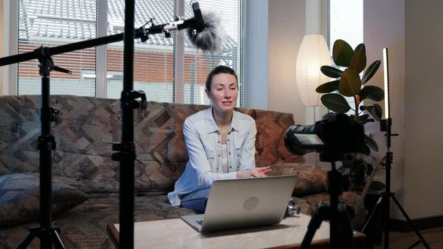 Woman blogger or vlogger streaming online on social media to her subscribers. Woman using microphone, video camera and other blogging set ups at her house while talking on camera.