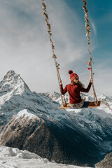 The girl sits on a swing in the mountains from the back. Heavenly swing over the abyss. 