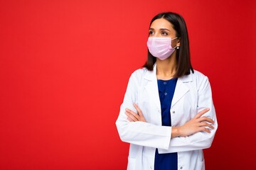 Young beautiful brunette woman in virus protective mask on face against coronavirus and white medical coat isolated on the background