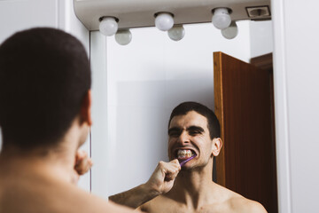 
young man brushing his teeth with a toothbrush in the bathroom at home