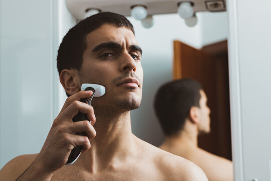 
young man shaving with an electric razor in the bathroom of his house