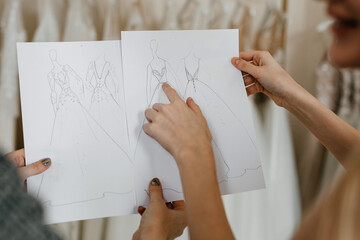 Fashion designer showing wedding dress sketches to a client at her studio.