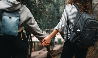 Two unrecognizable hispanic lesbian women in nature holding hands and hiking