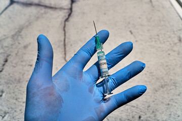 hand with a blue latex glove and one syringe in vertical position