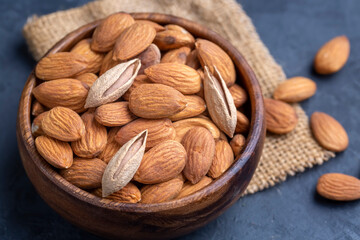 Almonds in brown wooden bowl on old wooden table background
