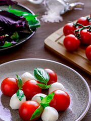 Caprese salad on round plate. Round tomatoes, mini mozzarella and green basil.
