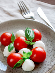 Caprese salad on round plate. Round tomatoes, mini mozzarella and green basil.
