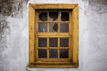 Retro style yellow window with shattered glass on dirty damaged white walls. Detail of window in abandoned rural house