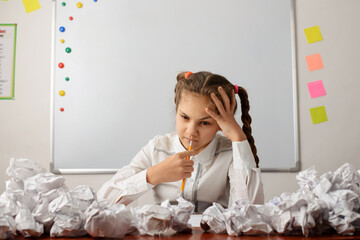 Secondary school learner thinking about some task, tries to do a home assignment, sitting in front of a board with many crumpled papers around. Thinking hard concept