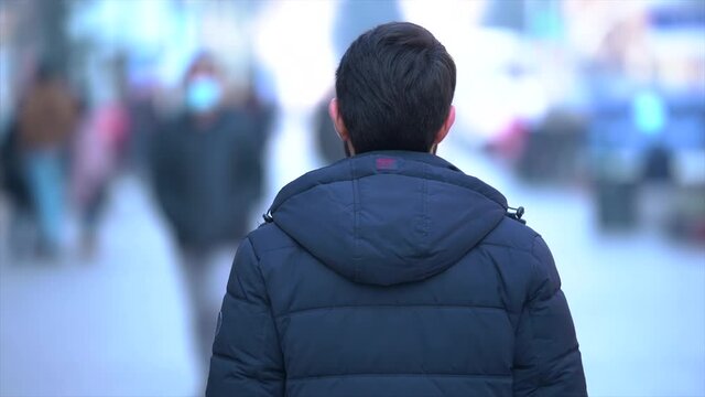  Time lapse back view man standing alone in the street,  while people are rushing around him.  In background people in medical masks walking on the street.  Quarantine, pandemic time. 