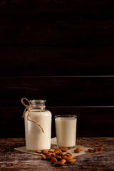 Almond milk in a bottle and a glass, on dark vintage wooden background, with copy-space