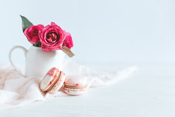 Tasty french macaroons with pink roses on a white background.