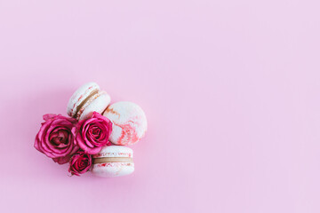 Tasty french macaroons with pink roses on a pink pastel background.