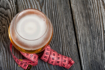 Beer in a glass and a measuring tape. On pine boards. A day without diets.