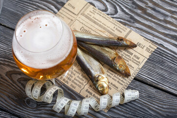 Beer in a glass and smoked fish. Nearby is a measuring tape. On pine boards. A day without diets.