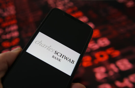 Viersen, Germany - February 6. 2021: Closeup of mobile phone screen with logo lettering of charles schwab bank, stock market chart background