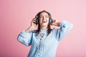 Joyful brunette girl listens to music on headphones in the studio on a pink background