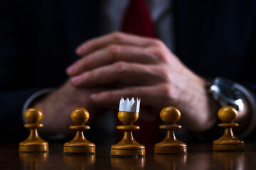 the concept of strategy and business planning, a businessman at a chessboard in front of lined up white pawns, one of which is in a paper crown, strategy and tactics, readiness for battle.
