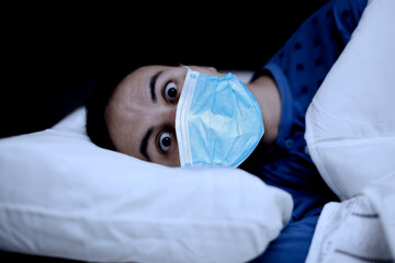 Portrait of an insomniac man in his bed while wearing a coronavirus covid mask