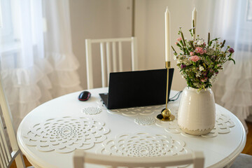 Home office. Laptop standing on the white round table. Beautifull bouquet of flowers and candles.