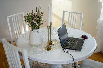 Home office. Laptop standing on the white round table. Beautifull bouquet of flowers and candles.