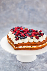 Delicious homemade heart shaped vanilla cake decorated with cream and fresh berries