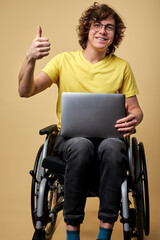 disabled man sits in a wheelchair with laptop, working online. curly young male in casual wear...
