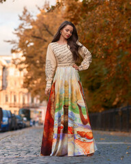 Elegant caucasian woman with long straight brunette hair in bright stylish colorful dress walking city street on a bright day