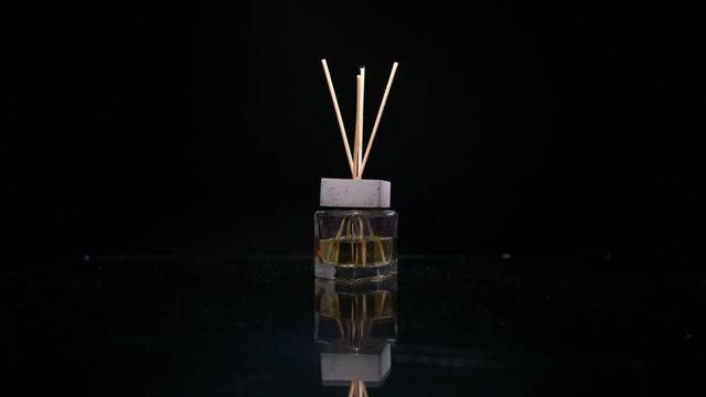 Female hand puts reed diffuser bottle on the mirror surface on black background