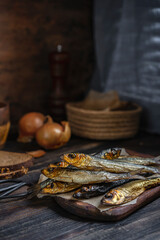 Cold smoked salaka with bread, onion ready to eat. Little golden fish close-up on dark wooden table, healthy natural sea food product, rich of essential Omega-6 fatty acids. Country fisherman style.