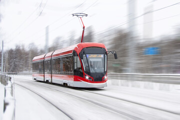 The tram is passing rapidly at a bend in a snow covered city park.