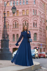 Fototapeta na wymiar Elegant caucasian woman with long straight brunette hair in blue and white stylish colorful dress walking city street on a bright day