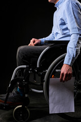 Obraz premium desperate disabled male sits with job search paper down, unhappy and hopeless. no social life and support. cropped man sitting on wheelchair