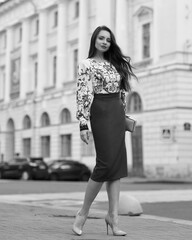 Elegant caucasian woman with long straight brunette hair in blue and white stylish colorful dress walking city street on a bright day