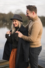 Gentleman covering his girlfriend with a jacket a cold autumn day on a pier