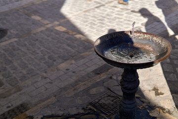 Fuente funcionando entre el sol y la sombra con un empedrado de la calle de fondo