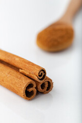 Cinnamon sticks with cinnamon powder in wooden spoon on white background.