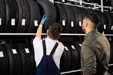 the seller offers new rubber wheels, tires, rims for the car. male client came to make purchase in auto service shop. auto mechanic showing assortment of tires © alfa27