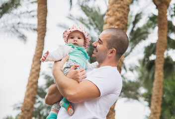 Father holds his charming newborn daughter under the palm trees