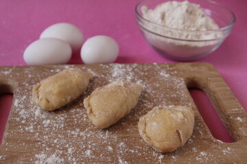 Fototapeta na wymiar Raw cooking dumplings lie on a board beside egg flour on a pink background view from above