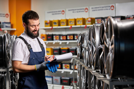 Male Salesman In Auto Shop Making Notes, Checking The Document And Examining Characteristics, Looking At Rack With Auto Rims