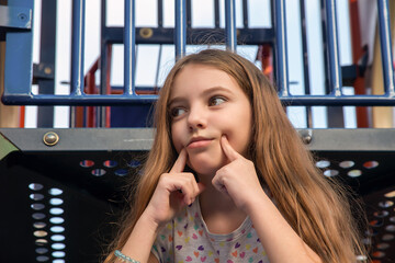 Beautiful emotional teenager girl sitting on the children's city playground on a sunny day